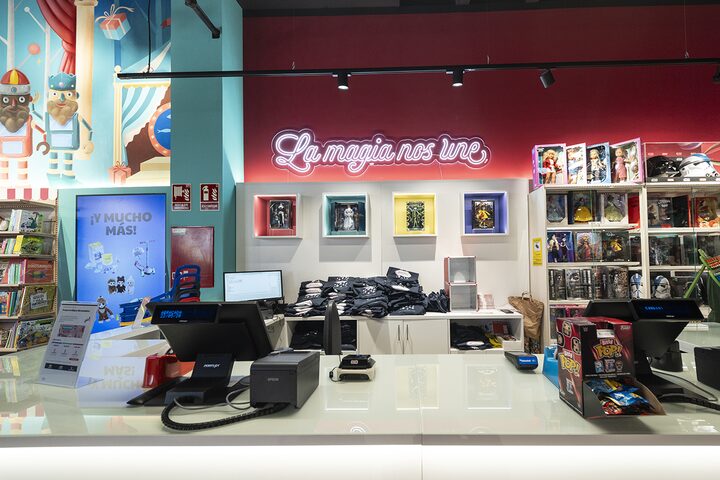 Mostrador de caja con r&oacute;tulo de ne&oacute;n "La magia nos une" y figuras de colecci&oacute;n en la jugueter&iacute;a de Puerto Venecia Abracadabra